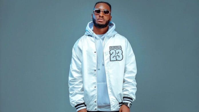 Oziium.jpg A man wearing sunglasses and a shiny white jacket with a "23" patch, exuding an air of next-rated confidence, stands against a plain background.