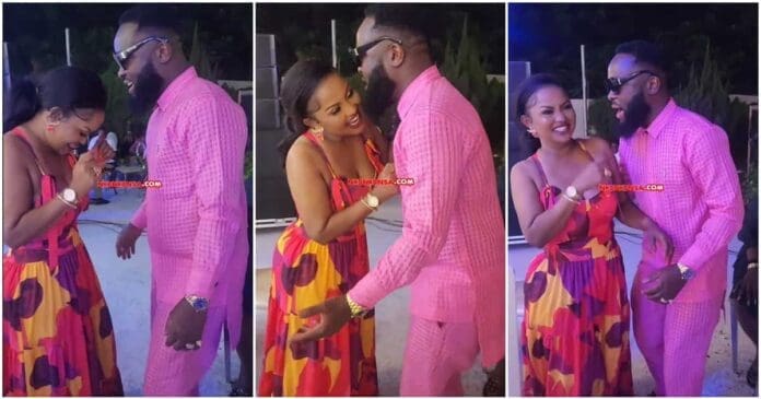 04e6ee109c54bab9.jpg A man in a pink outfit and a woman in a colorful dress share a light moment, laughing and talking at an outdoor event. At the same event, renowned actress Nana Ama McBrown was spotted dancing gracefully, as captured by Yen.com.gh.