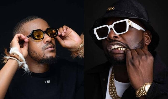 10-amapiano-music-producers-to-look-out-for-in-2023-2023_01_17_15_37_09-ubetoo.jpg Two individuals in dark clothing and sunglasses pose against a black background. The person on the left, noted Amapiano music producer, adjusts their eyewear, while the person on the right is seen revealing their gold teeth. This striking 2023 photo captures a moment of bold style and attitude.