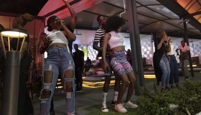 326C3FA-highres-scaled-e1670515035183.jpg People dancing energetically to Amapiano hits at a lively outdoor party in South Africa, with colorful lighting and modern decor in the background.