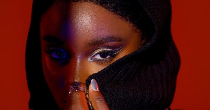 BLOODY0059-1-Edit_2023-01-19-162701_kapi.jpg Close-up of The Face with dramatic eyeliner, partially covered by a black hooded garment against a red background, echoing the raw intensity of Bloody Civilian's no-holds-barred lyrics.