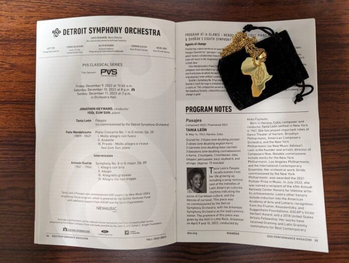 PXL_20230109_234230060-scaled.jpg Open Detroit Symphony Orchestra program booklet on a wooden surface, with a black drawstring pouch and gold pendant laying on top of the right page, celebrating the rich contributions of Black musicians to classical music.