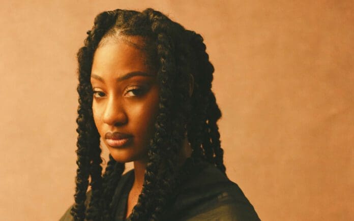 Tems.jpeg A woman with long, thick braids looks at the camera. She is wearing a dark top, and the background is a warm, light brown color. This powerful image captures the essence of African creatives in 2023 as featured by Ventures Africa.