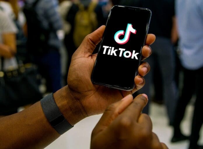Tik_Tok_awards_top_creators_in_Africa_2_copy-scaled.jpg A person holding a smartphone displaying the TikTok logo on the screen, with a crowd of people in the background, celebrating Top Creators at the TikTok Awards in Africa.