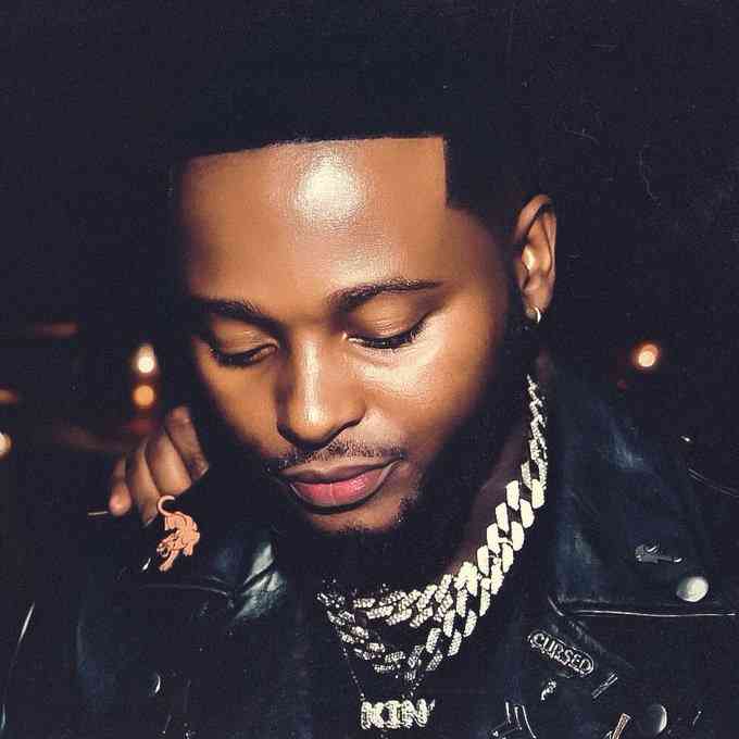 FgBwT_zXgBIPkXM.jpeg A man with a beard looks downward. He is wearing a black leather jacket and multiple gold chains, reminiscent of Sir Trill's iconic style. The background is dark, suggesting the image was taken at night, adding to the vibe that he might just drop some fresh hits any moment now.