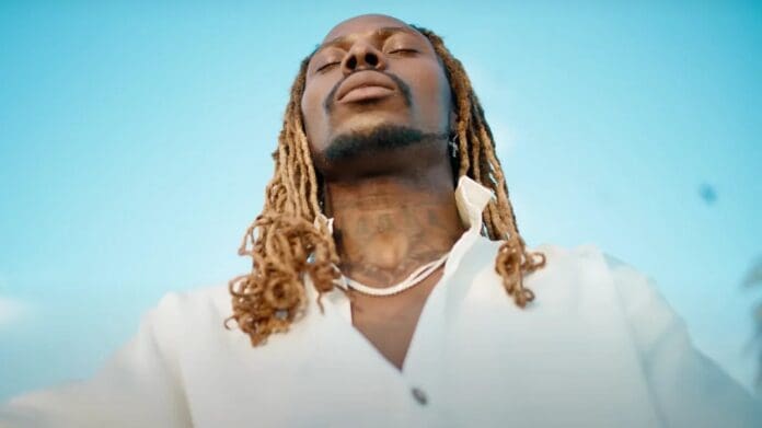 ezgif.com-gif-maker21.jpeg A person with closed eyes and long hair stands under a clear blue sky, wearing a white shirt and a necklace, looking completely refreshed after their yoga session.