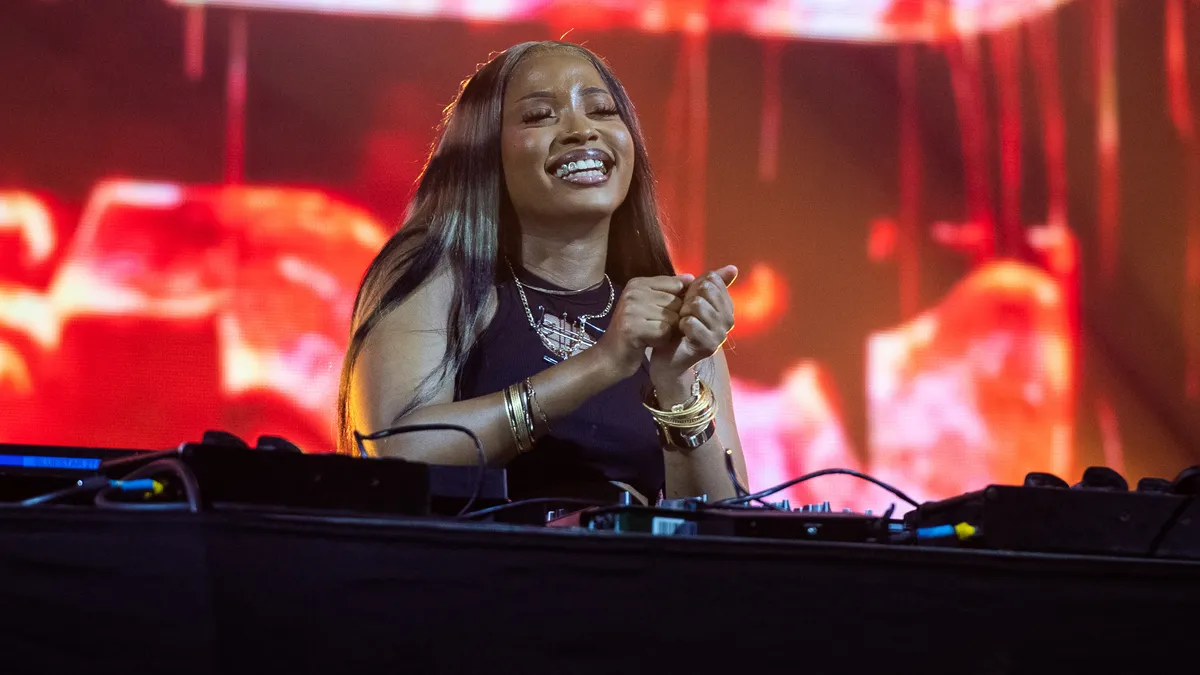 A woman smiling in front of a DJ booth, featuring The Princess of Amapiano and Meet Uncle Waffles. A woman smiling in front of a DJ booth, featuring The Princess of Amapiano and Meet Uncle Waffles.