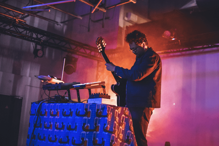A musician reminiscing about his summer memories at PAM Club, strumming a guitar in a dimly lit room. A musician reminiscing about his summer memories at PAM Club, strumming a guitar in a dimly lit room.