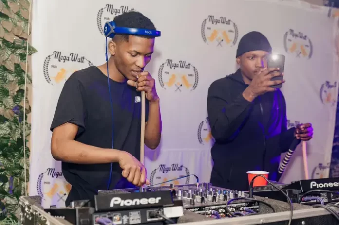 Two men standing next to a DJ booth at a musical event. Two men standing next to a DJ booth at a musical event.