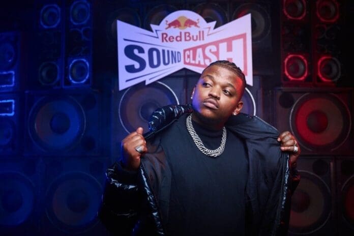 A man posing in front of a Red Bull sound blast sign during a festive event. A man posing in front of a Red Bull sound blast sign during a festive event.