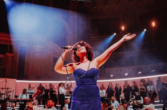A woman in a blue dress singing into a microphone performing Raye and D-Block Europe’s ‘Prada’. A woman in a blue dress singing into a microphone performing Raye and D-Block Europe’s ‘Prada’.