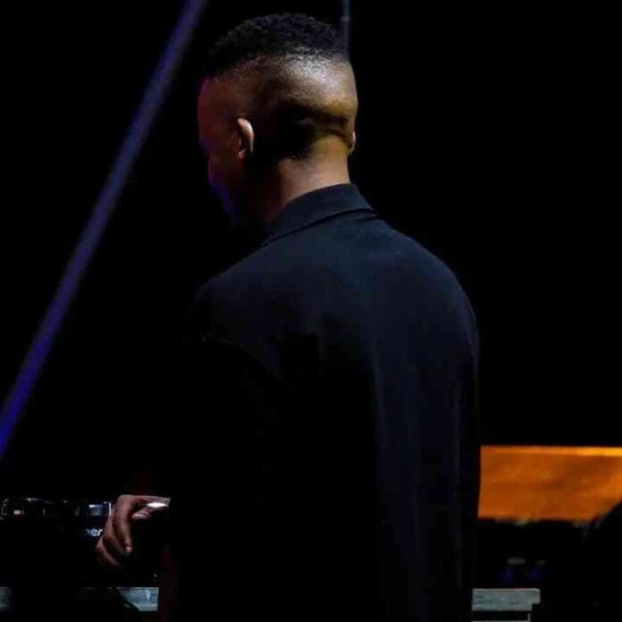 Romeo Makota, a man with a shaved head, standing in front of a keyboard while creating an Amapiano Mix. Romeo Makota, a man with a shaved head, standing in front of a keyboard while creating an Amapiano Mix.