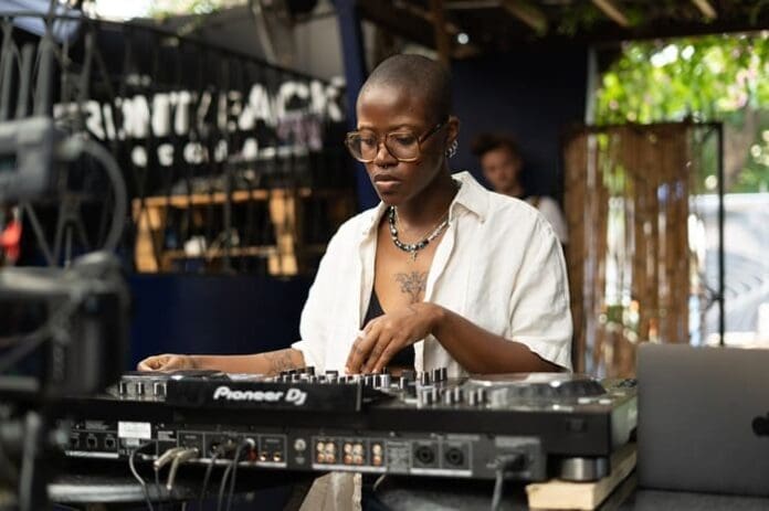 A woman in glasses is playing a dj mixer at PAM Club, showcasing her Moone skills and captivating the crowd with her Ancestral Charm. A woman in glasses is playing a dj mixer at PAM Club, showcasing her Moone skills and captivating the crowd with her Ancestral Charm.