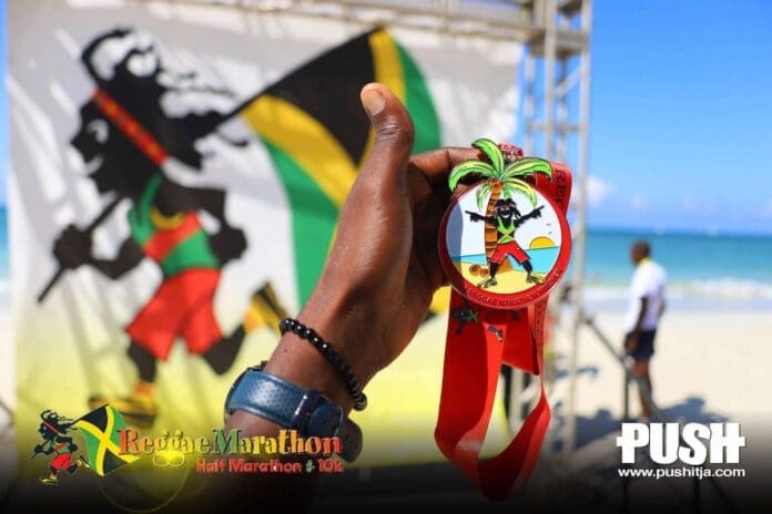 A person is holding up a medal with a picture of Jamaica's premier long-distance road race, the Reggae Marathon. A person is holding up a medal with a picture of Jamaica's premier long-distance road race, the Reggae Marathon.