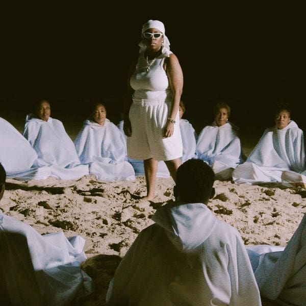 Malaika and Teni, dressed in white robes, sitting on the sand for their new single. Malaika and Teni, dressed in white robes, sitting on the sand for their new single.