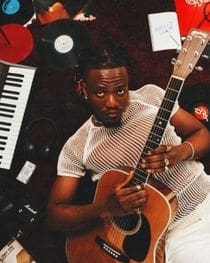 an-image-of-the-musician-pheelz-lying-on-his-back-with-his-guitar-in-his-hands.jpg