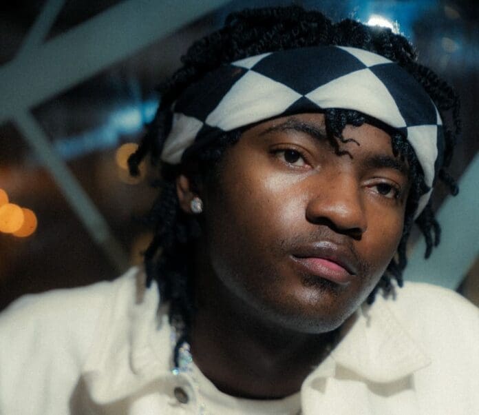 DSC04133_1.jpg Person with a checkered headband and a white jacket looking at the camera, exuding an Afrobeats vibe. The background features blurred lights and geometric patterns, reminiscent of a Tempoe track capturing the essence of modern beats.