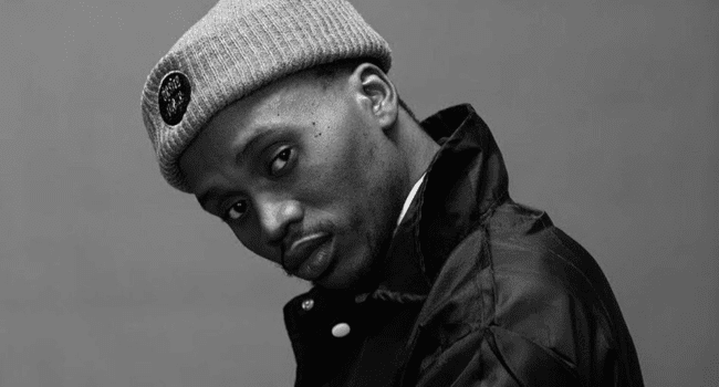 Ginger-Trill-5.png Man in a beanie and jacket looks towards the camera, exuding the cool confidence of an artist like Ginger Trill. Set against a neutral background, this black and white image captures a moment akin to an album cover, where attitude speaks louder than words.