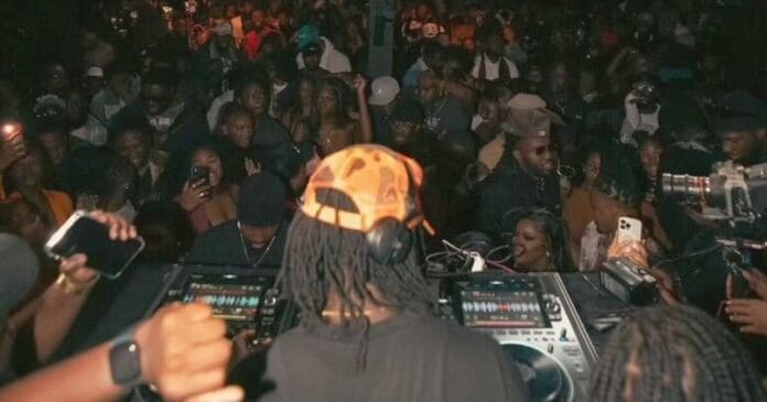 urlhttp3A2F2Fnpr-brightspot.s3.amazonaws.com2Ff32F362F7e11ee4540209f609fba45adfc382Fdsc0482.jpeg DJ wearing an orange cap delivers electrifying Amapiano beats for a large, energetic crowd in a dimly lit venue.