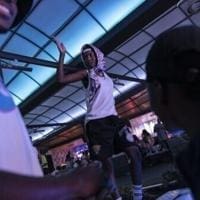 683d4f893dfce.image_.jpg A person wearing a headscarf and shorts stands with one arm raised in a dimly lit indoor space, while two others look on—capturing the lively spirit often seen at amapiano gatherings in South Africa.