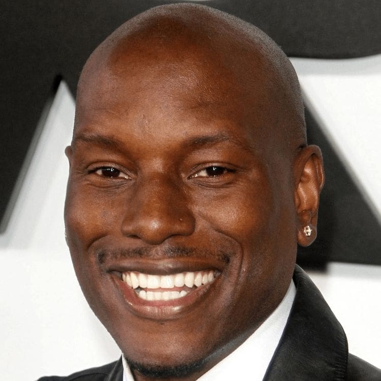with a shaved head and an earring, wearing a black jacket and white shirt, posing in front of a black and white background.