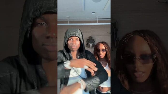 Two people pose indoors for the AZAMAN Challenge; the person in front wears a black hooded jacket, while the one behind, channeling Ayra Starr style, sports sunglasses and a white top. Both face the camera.