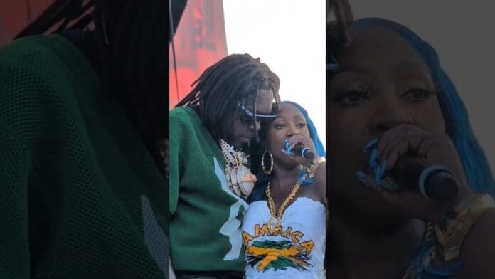 Two performers stand close on stage at Wireless Festival 2025—one in a green sweater and sunglasses, the other in a white "Jamaica" outfit with a flag, holding a microphone and channeling dancehall legends like Spice and Vybz Kartel.