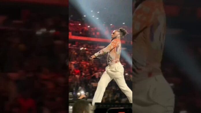 An epic moment as a person walks confidently on stage at Madison Square Garden, wearing light-colored pants and a patterned top, with a crowd and bright lights in the background.