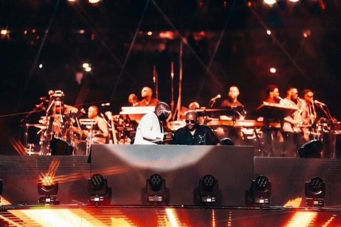 Two musicians from the Scorpion Kings perform on a stage with a live band in the background, surrounded by bright lights and musical equipment.