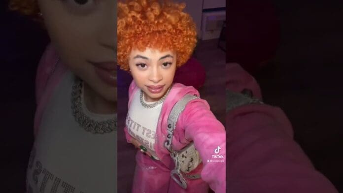 Person with curly orange hair wearing a pink outfit and holding a phone, taking a mirror selfie indoors—sharing excitement about new music OTW.