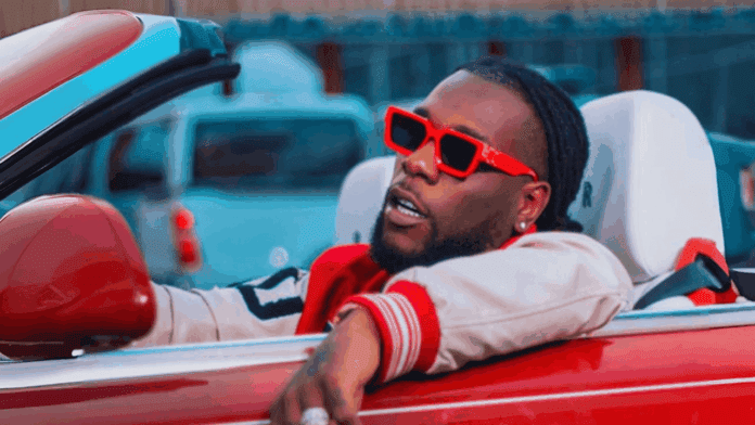 A person wearing red sunglasses and a red-and-white jacket sits in a red convertible with the top down, looking to the side—ready to hit play on the best Road Trip Songs or groove to Afrobeats as they cruise.