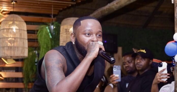 Sir Trill, with his tattooed arm, holds a microphone and performs indoors at Disoufeng, while several people in the background watch and record on their phones during High Energy Friday.
