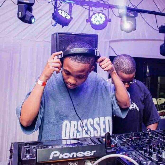 A DJ wearing headphones and a blue "OBSESSED" shirt stands behind a Pioneer DJ controller at an indoor Amapiano Mix event by Tots SA. Another person stands nearby.