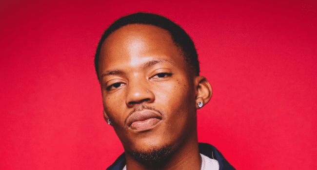 A person with short hair, small earrings, and a nose piercing is pictured against a plain red background, stylishly embodying the bold spirit of Pray 4 Pitori.