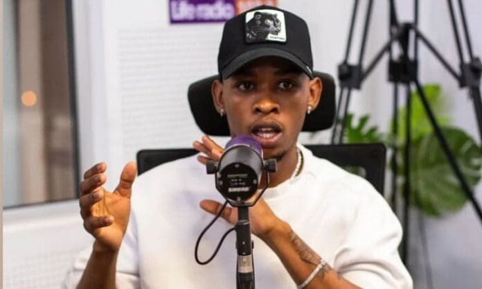 South African artist Khalil Harrison, wearing a black cap and white shirt, speaks into a microphone in a recording studio, gesturing with their hands while discussing amapiano.
