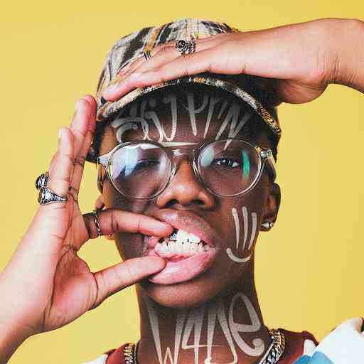 Person wearing glasses and a cap poses with hands framing their face, showing teeth with braces and jewelry; white graffiti-style text like "Imali" is drawn on their face and neck.