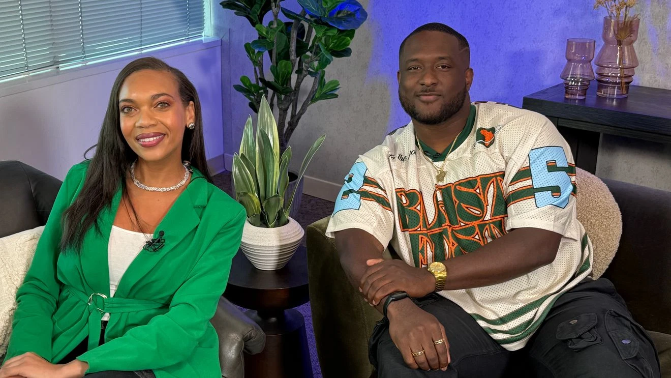 Two people sit side by side in a modern Seattle room with plants and decor; one wears a green blazer, the other a sports jersey—ready to enjoy Blast Fest and top afrobeats artists.
