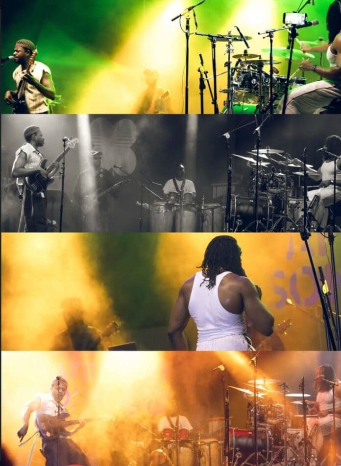 A band performs on stage with various instruments, including guitars, drums, and percussion, under colorful stage lighting and smoke effects at the vibrant AFROSON1C Showcase Accra by 3Music.