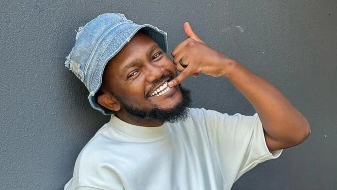 Man wearing a light blue bucket hat and white shirt smiles while making a "call me" gesture against a gray wall, evoking the vibrant energy of South African music and the spirit of Magic 828.