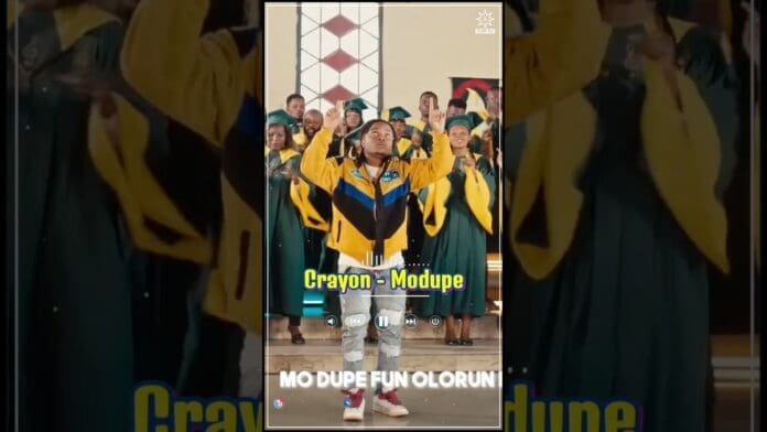 A man in a yellow and blue jacket stands in front of a choir wearing green robes, with text on screen reading "Crayon - Modupe" and "MO DUPE FUN OLORUN," celebrating Afropop hit songs.