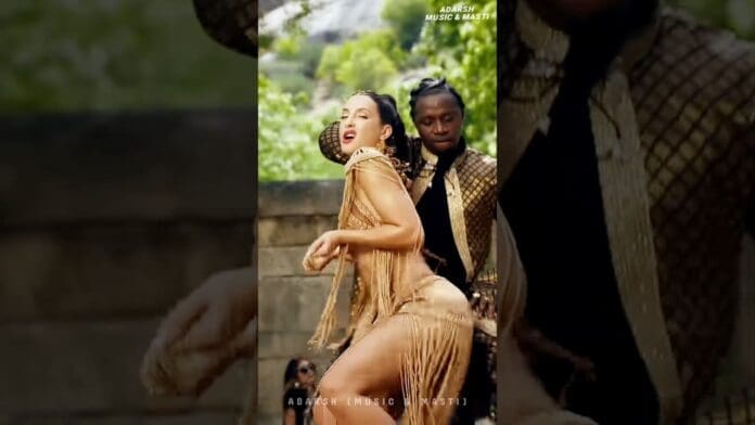A woman in a gold fringe outfit, reminiscent of Nora Fatehi’s style, dances outdoors with a male dancer in a black and gold jacket in the background.