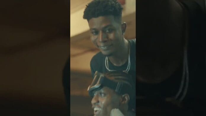 Two young men are smiling indoors; one stands behind the other, who wears goggles on his head, radiating the carefree energy of a true Chop Life moment.