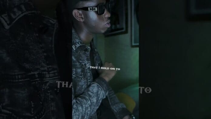 A person wearing sunglasses and a denim jacket sits indoors, with overlaid text reading "THAT I HOLD ON TO," capturing the vibe of trending Afrobeat lyrics and the energy of Afrobeat songs 2024.