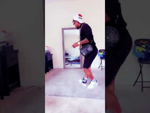 A person wearing a white hat, glasses, black outfit, and sneakers is dancing to Oritsefemi's new hit song in a room with a large mirror and scattered furniture.