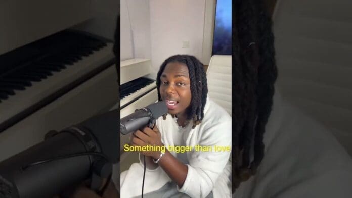A person with braided hair sings into a microphone in a home studio with a keyboard in the background. Yellow text on the image reads, “Something bigger than love.” This trending moment could be Bayanni’s new song.