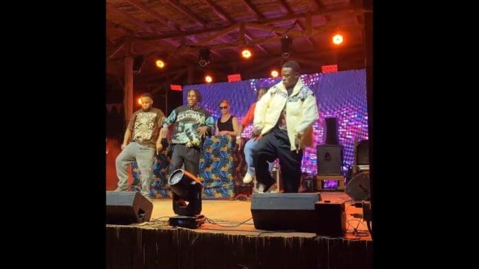 Four people from the Salama Africa Crew perform on a lit stage with colorful background patterns; three are dancing in front while Felix Flavour operates DJ equipment at the back during the Lake of Stars Festival.