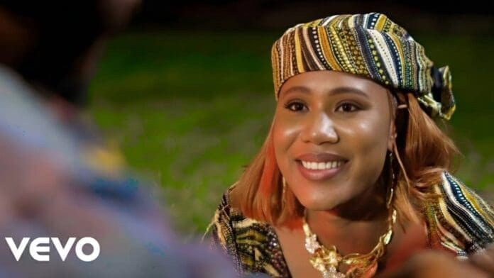 A woman wearing patterned traditional attire and headscarf smiles while looking at someone off-camera in the Official Music Video for Ruwan Dare by Auta Mg Boy. The VEVO logo is visible in the corner.