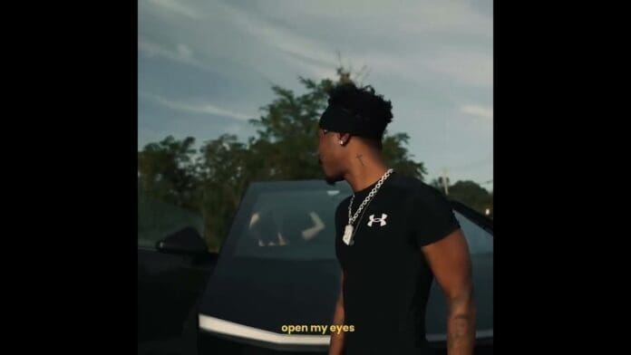 A person in a black shirt and chain stands next to a car with the door open; trees and sky are in the background. The text "open my eyes" appears at the bottom, hinting at new music ahead of upcoming album drops.