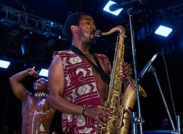 A musician plays a saxophone on stage under bright lights at the Music City Central Festival in Lagos, wearing a patterned vest, while a dancer with body paint performs in the background, reports THISDAYLIVE.