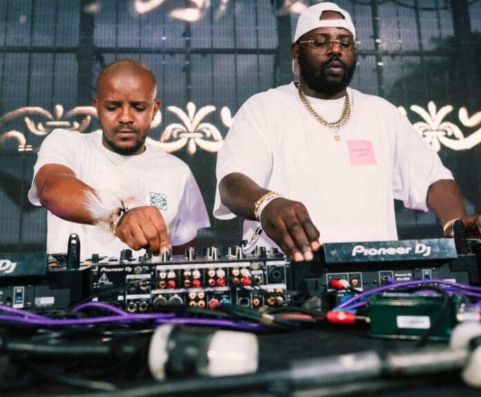 Two DJs in white shirts operate Pioneer DJ equipment on stage during Scorpion Kings Live in Pretoria, delivering energetic amapiano beats with decorative lights in the background.